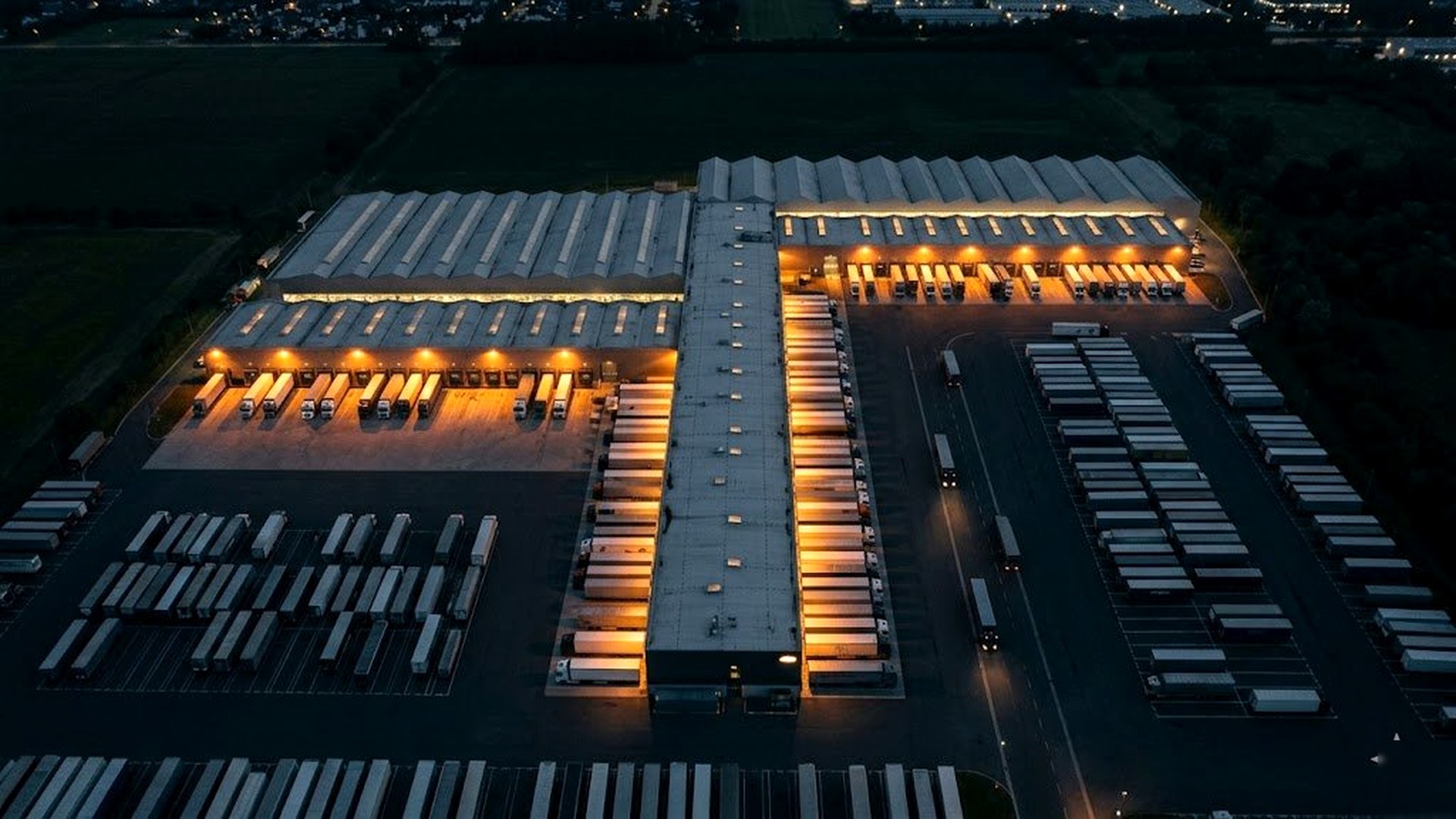 Aerial view of a freight cross-dock facility at night, lit by amber dock lights